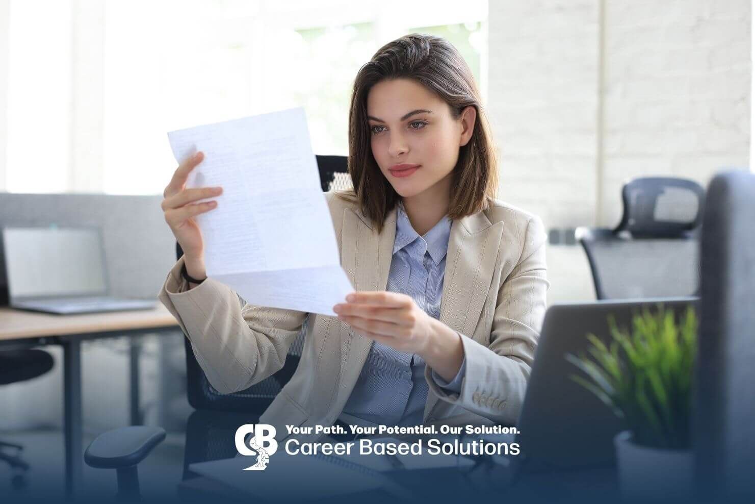 A therapist sitting at a desk in a modern office, reviewing documents while using a laptop.