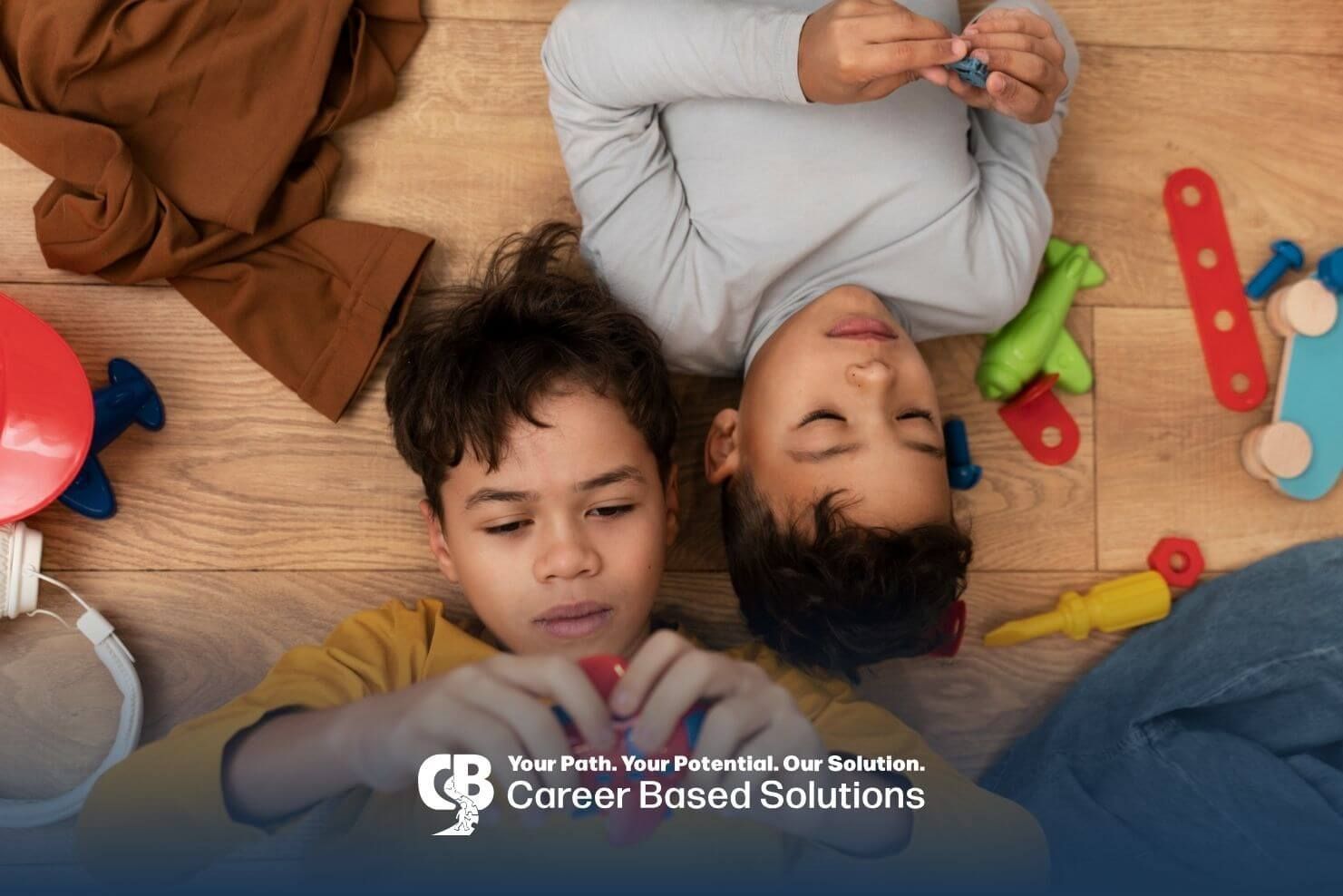 Two autistic young boys lying on wooden floor playing with colorful toy airplane and blocks.