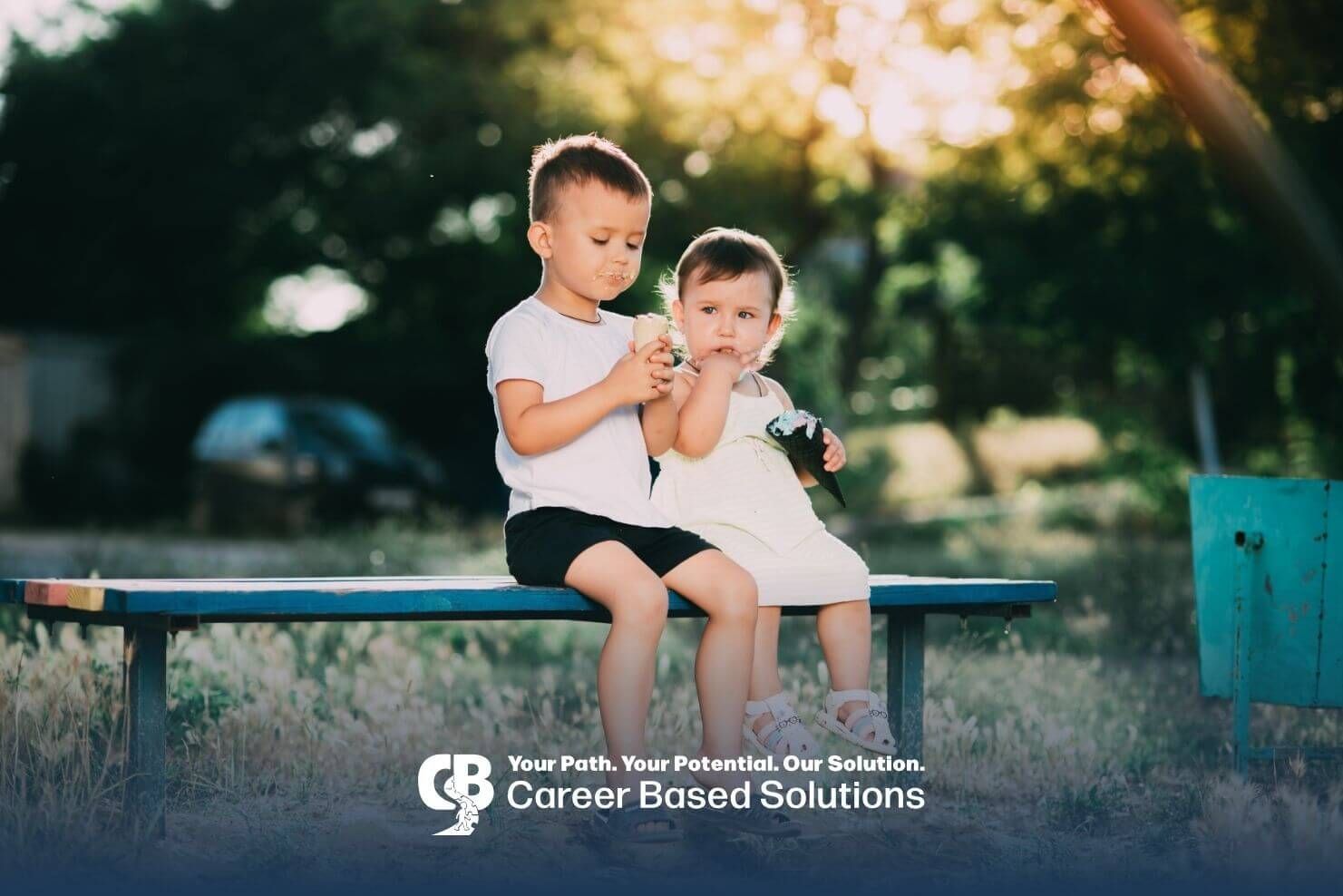 Two small autistic children sitting on a bench outdoors eating ice cream cones on a sunny day.