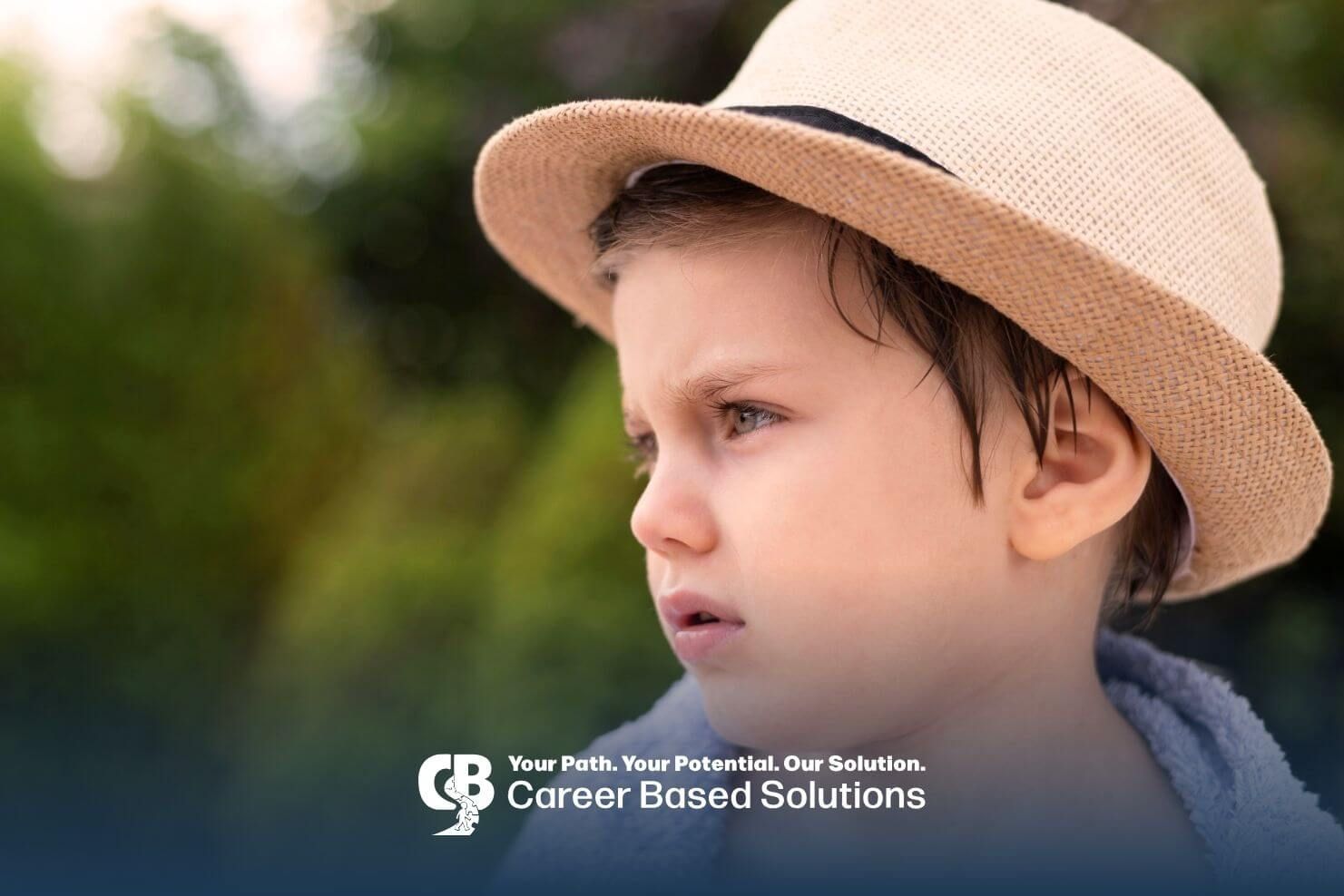 Autistic boy outdoors in summer hat looks concerned, showing sensory or routine challenges.