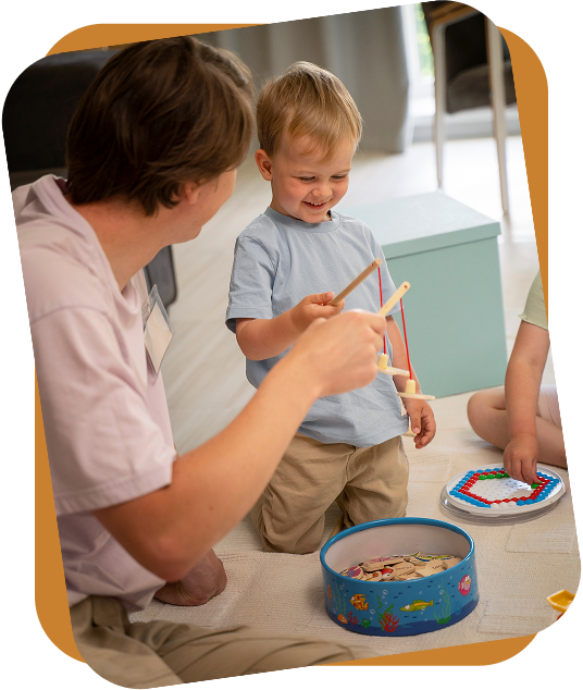 An RBT shows three flashcards featuring clothing items to a child sitting on a rug in a bright room.