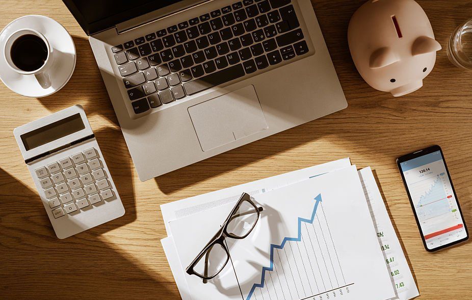 Image of a desk with laptop, paperwork showing growing investments, a calculator, and coffee