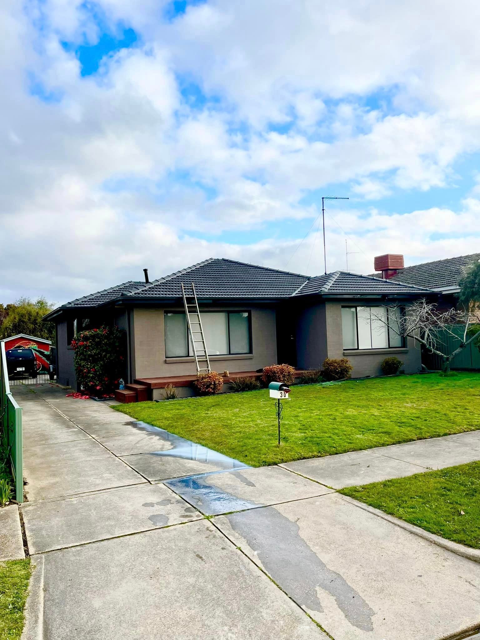 A house with a ladder on the roof and a lawn in front of it