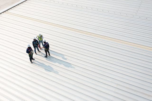 a group of construction workers are standing on top of a white roof .