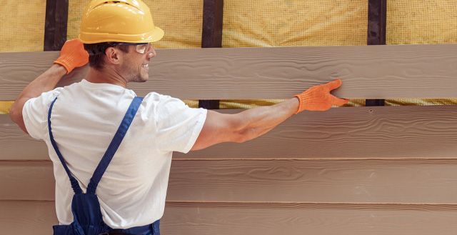 a man wearing a hard hat and gloves is working on a wooden wall .