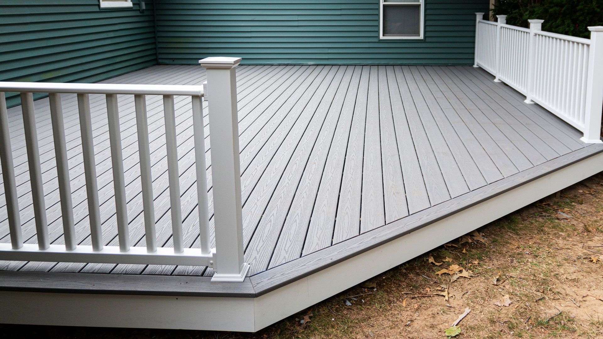 a gray deck with a white railing and a green house in the background .