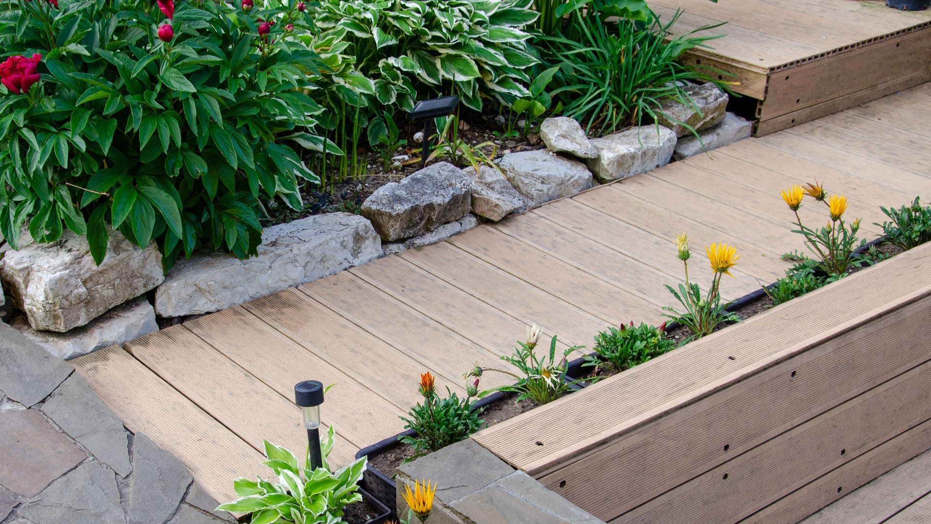 a wooden walkway leading to a garden with flowers and rocks .