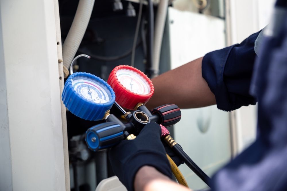 HVAC technician using gauges to inspect an air conditioning unit. Blue and red gauges, black gloves.