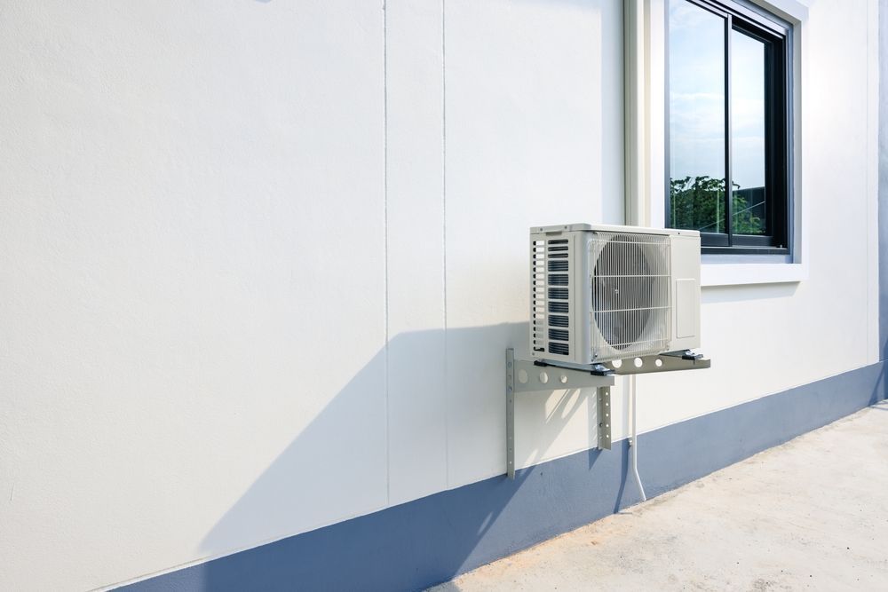 White air conditioning unit mounted on a white and blue building wall near a window.