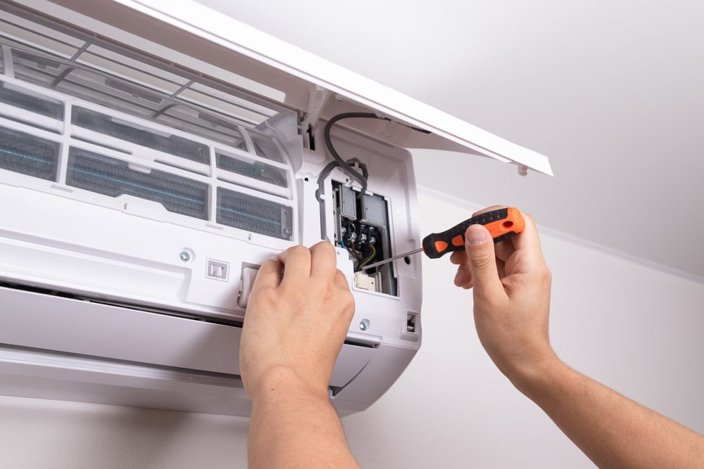 Person repairs a white air conditioner with a screwdriver.