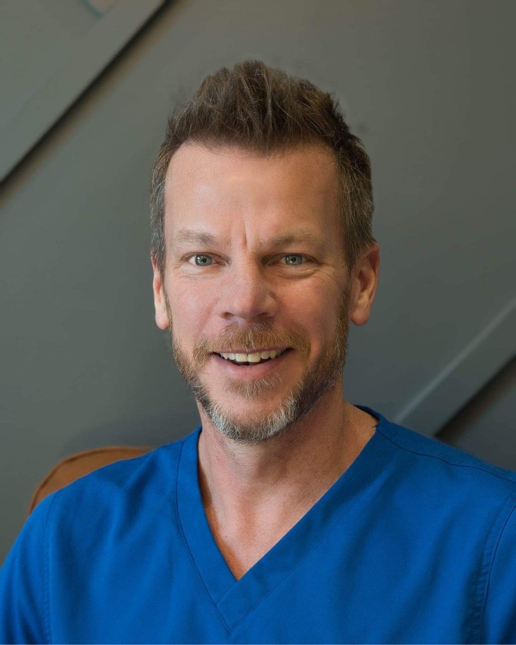 A man with a beard wearing a blue scrub top is smiling for the camera.