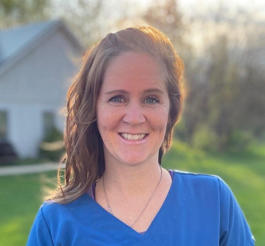 A woman in a blue scrub top is smiling for the camera.