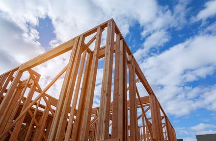 Wooden framing of a building under construction against a bright blue sky with scattered clouds.
