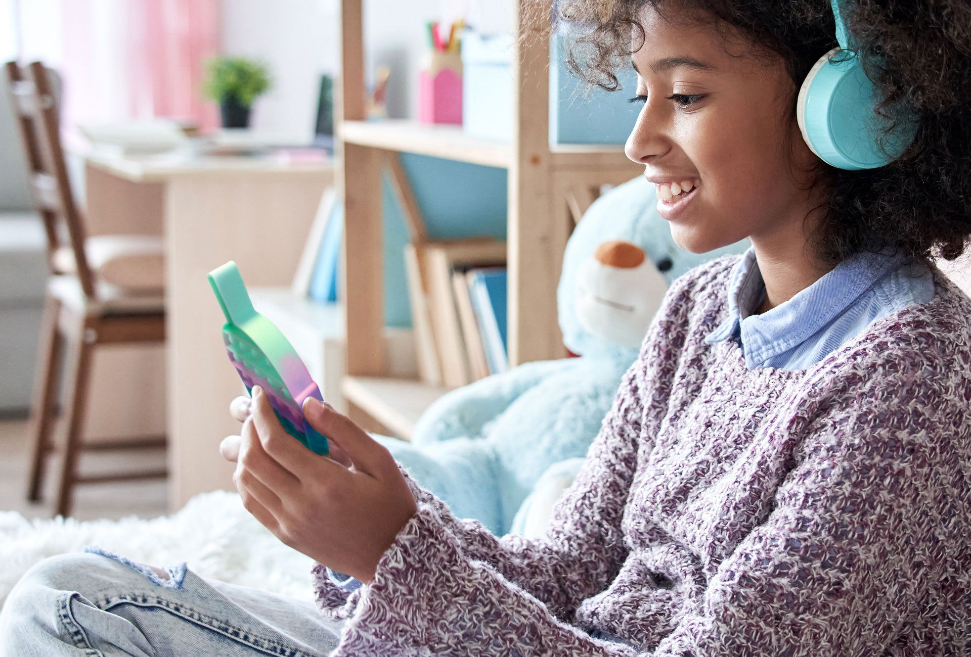 A young girl wearing headphones is sitting on the floor holding a cell phone.