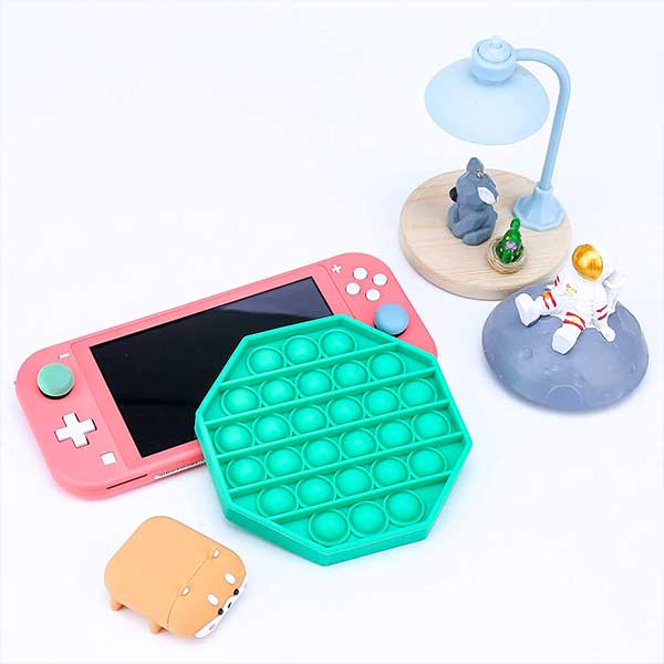 A pink nintendo switch lite is sitting next to a green pop it.