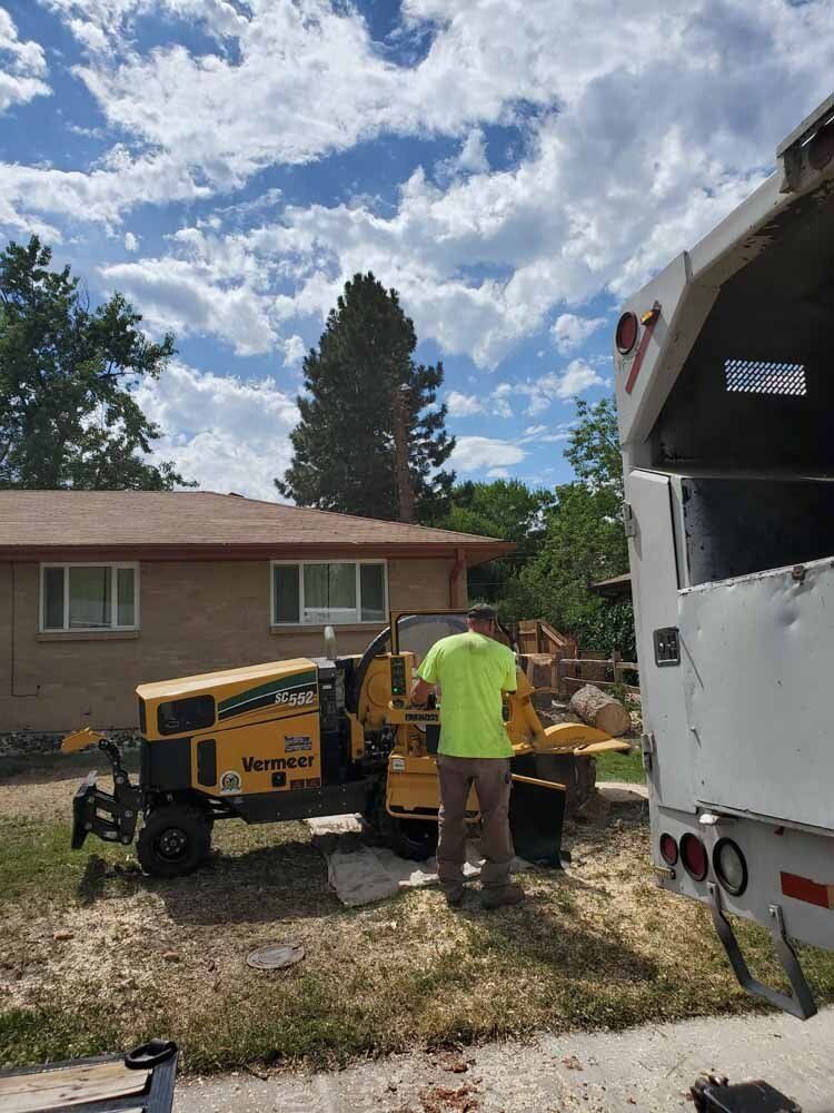 A man is working on a tree stump grinder in front of a house.