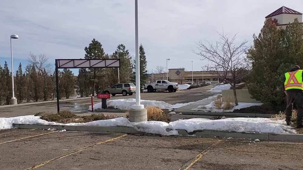 A man in a yellow vest is walking through a snowy parking lot.