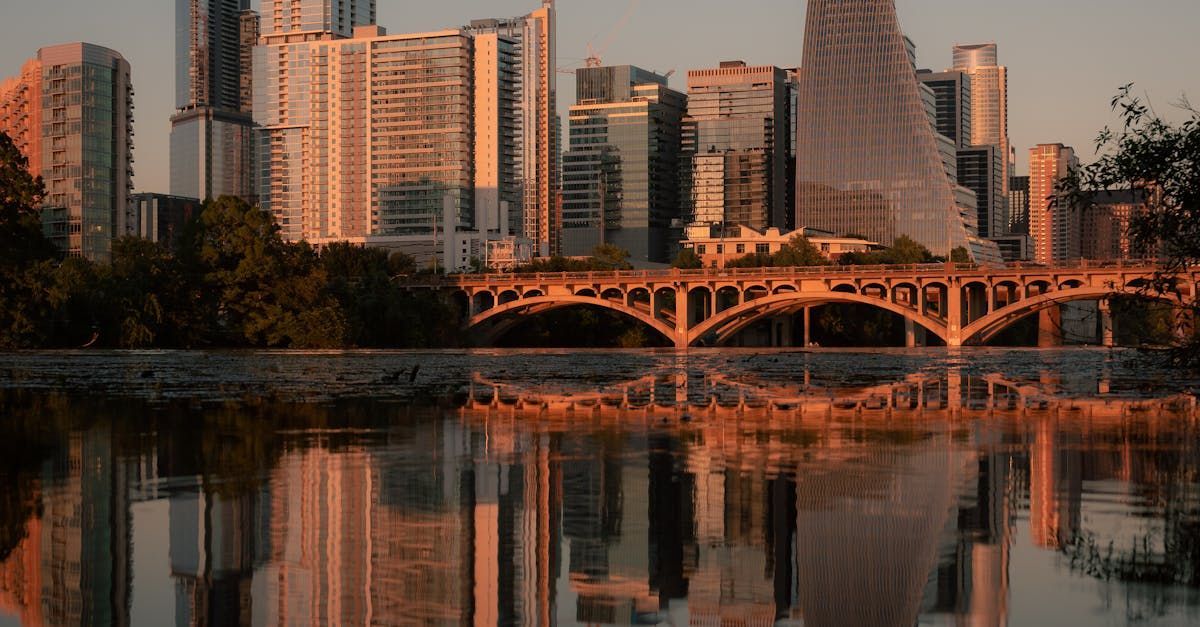A city skyline is reflected in a body of water with a bridge in the foreground.