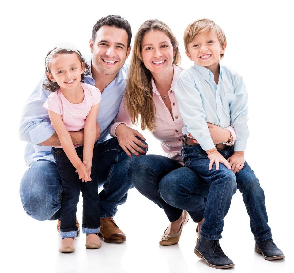 Famiglia di quattro persone sorridenti, accovacciate, davanti a uno sfondo bianco. Indossano abiti casual; i genitori hanno figli.