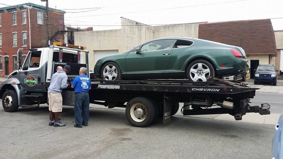 A green car is being towed by a tow truck