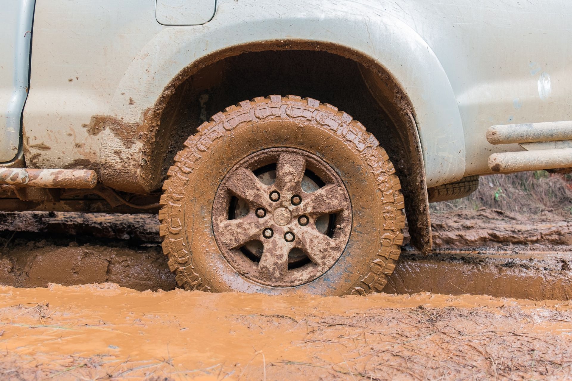 A muddy truck is driving through a muddy puddle.