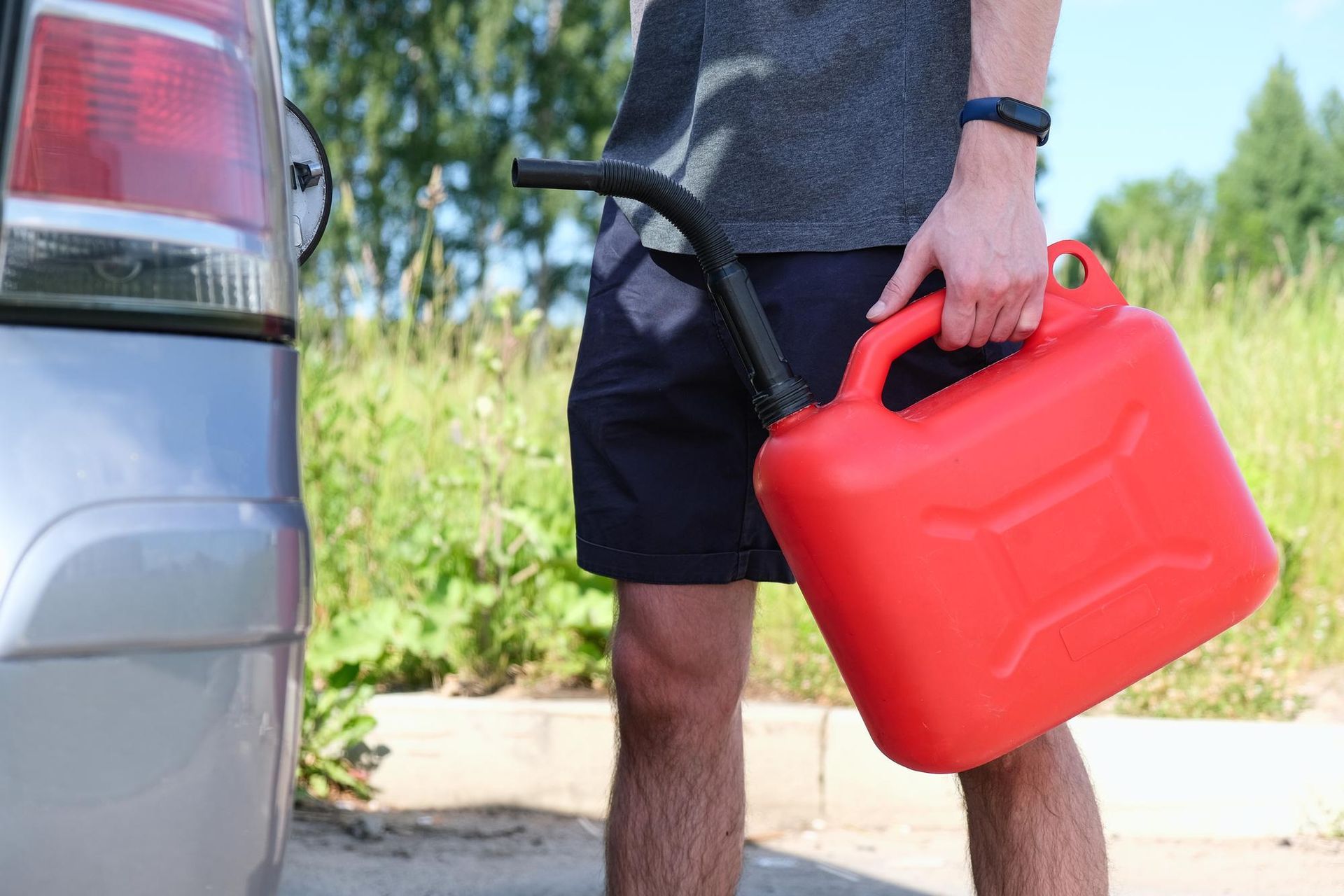 A man is holding a red gas can next to a car.