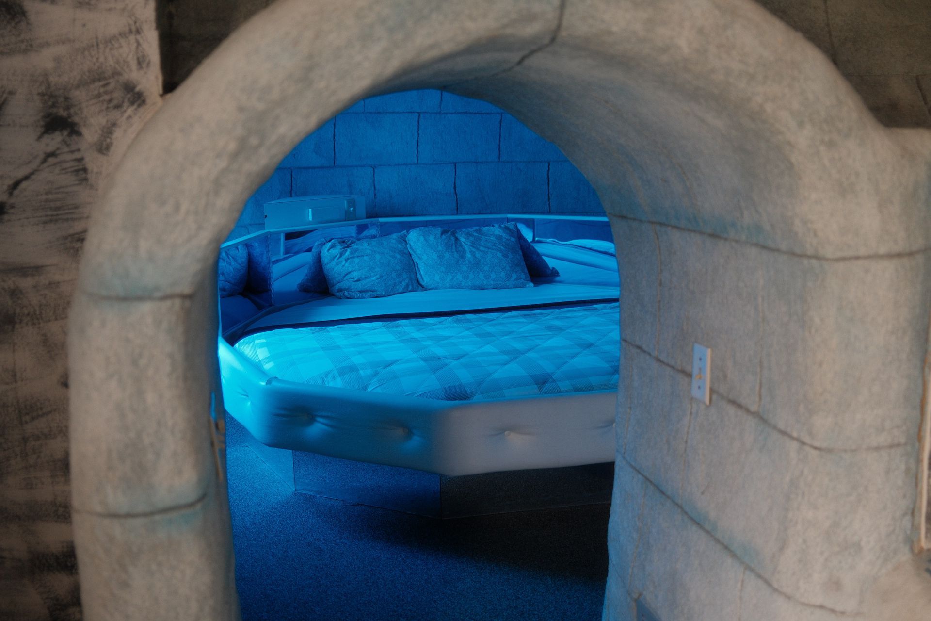 A bed in a room with a blue light coming through an archway.