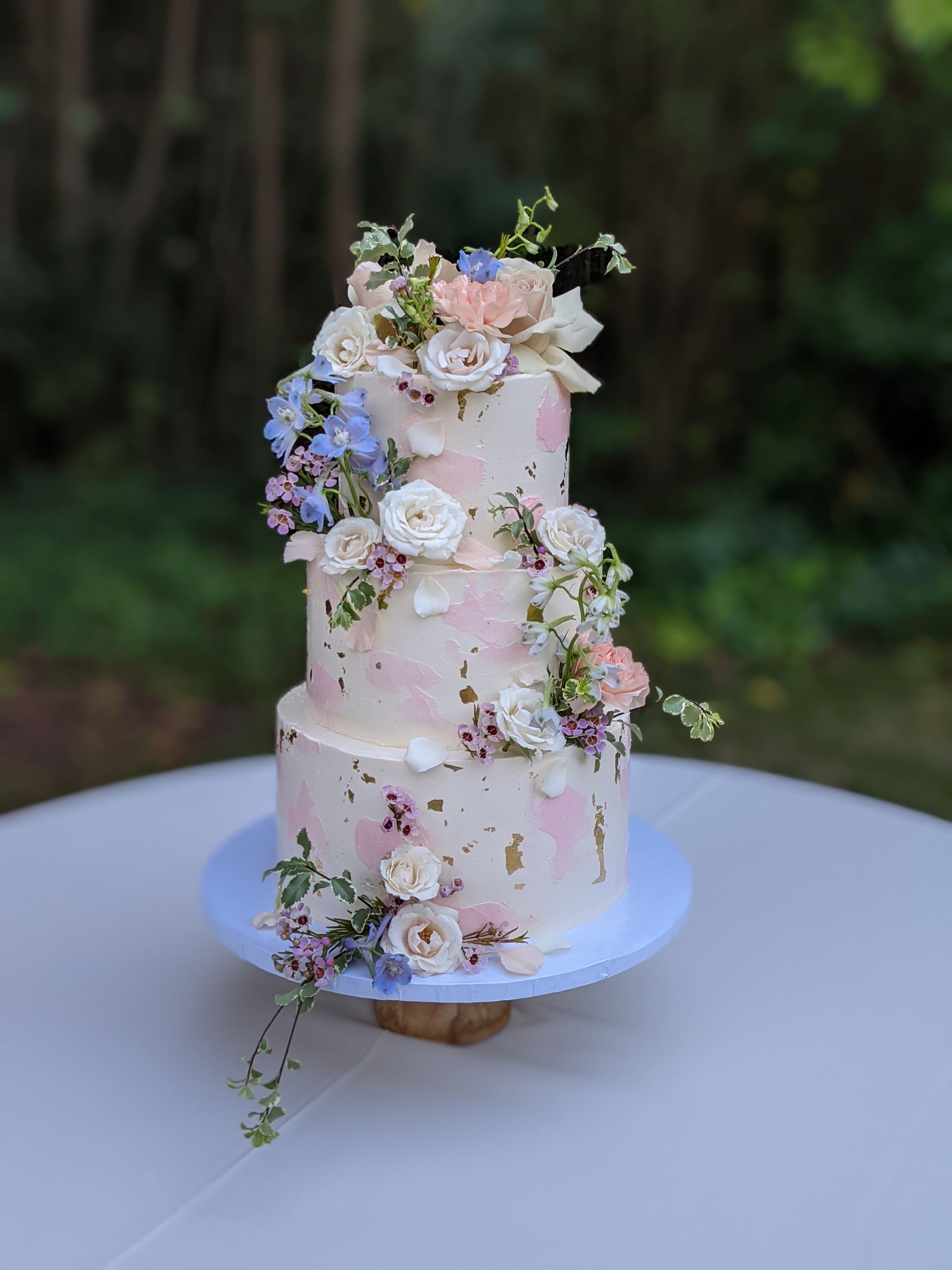 Three-tiered wedding cake, whimsically designed with blush buttercream accents and fresh florals
