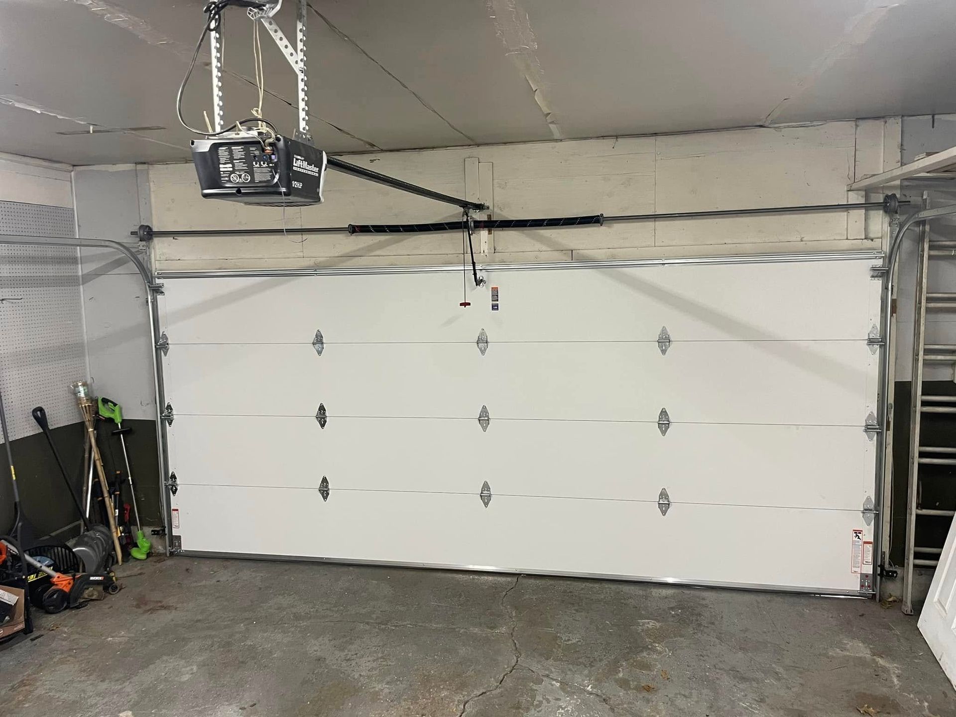 Interior of a garage with a white sectional door, concrete floor, and ceiling-mounted opener
