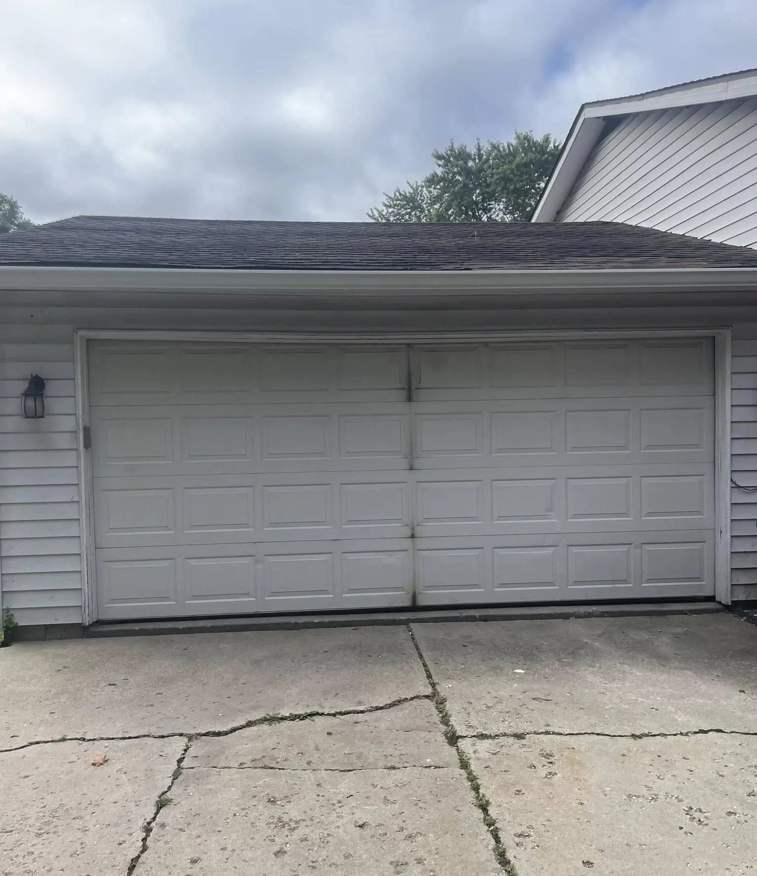White double garage door on a house with cracked concrete driveway and cloudy sky above