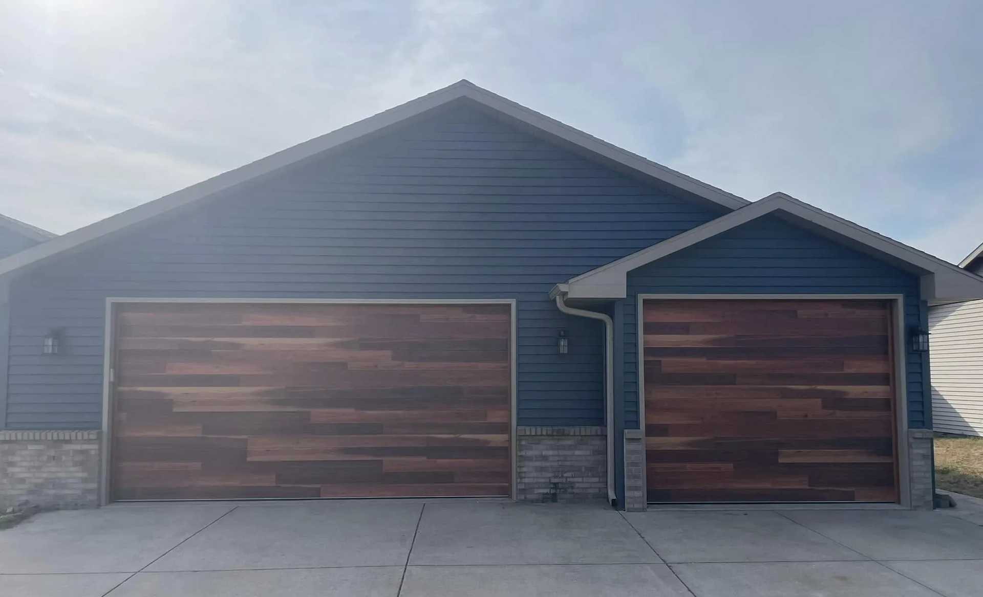 Blue-gray house with two wooden garage doors and a concrete driveway