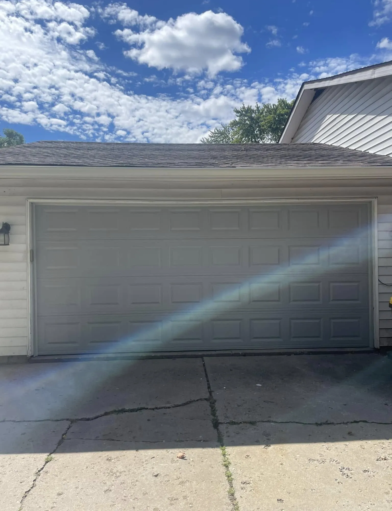 Two-car garage with gray doors, cracked driveway, and blue sky with clouds.