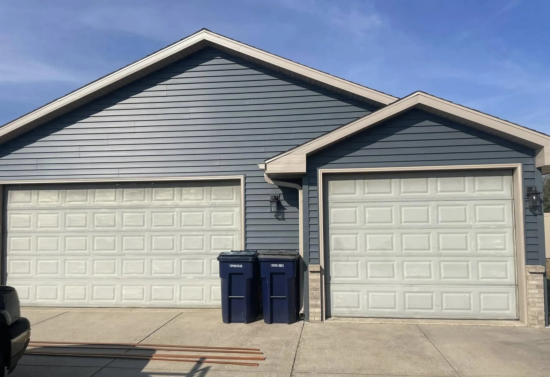 Two-car gray garage with blue trash bins on a concrete driveway under a clear sky