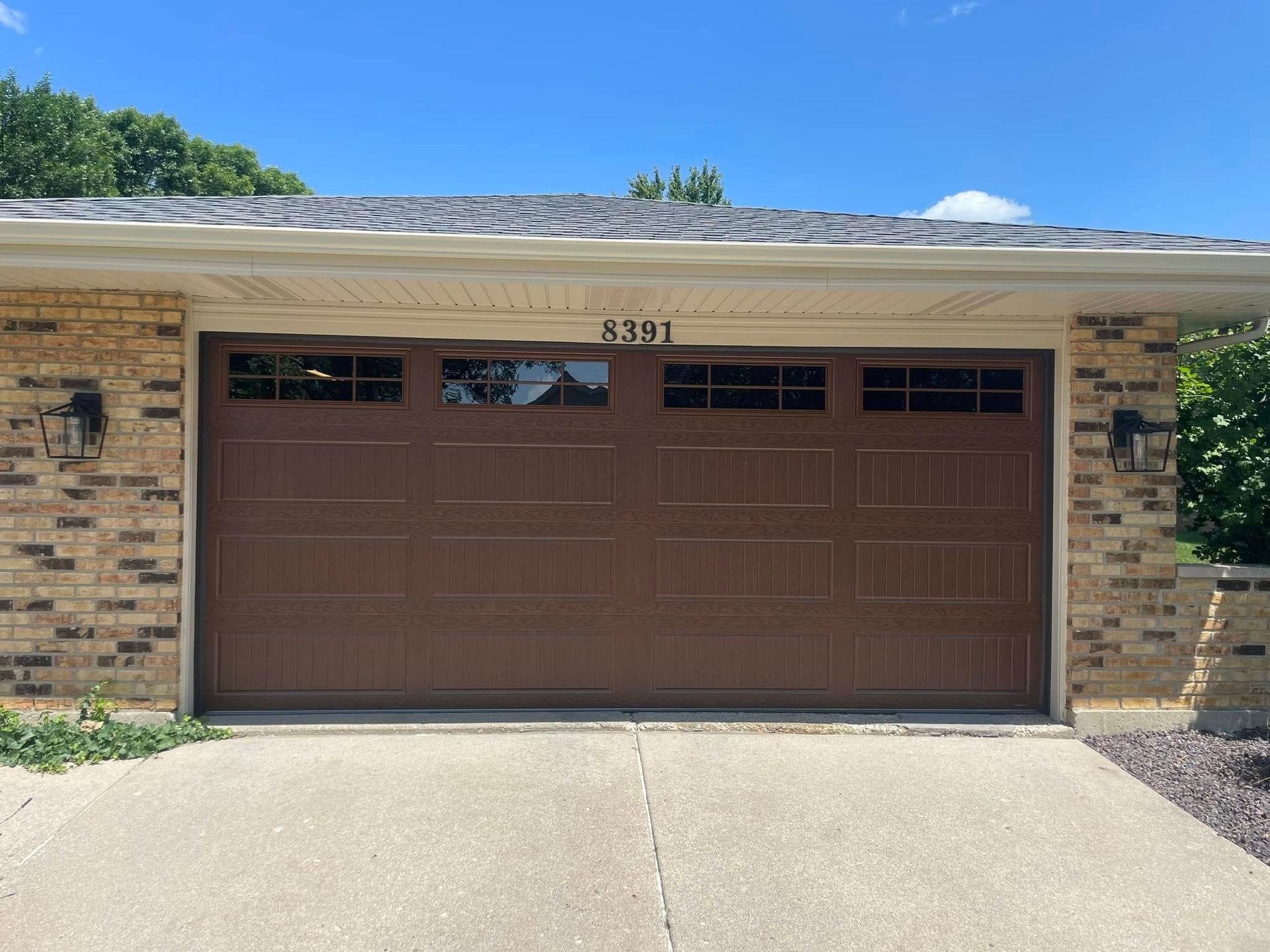 Brown double garage door on a brick house under a bright blue sky.