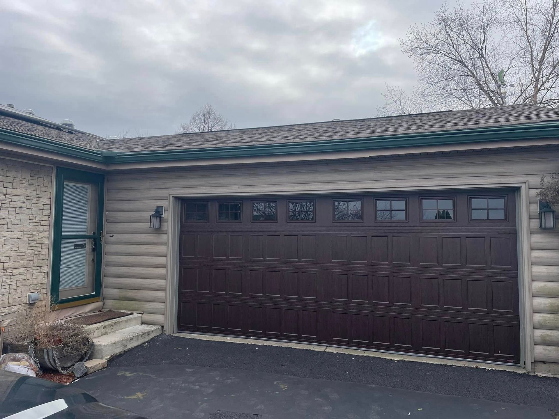 Stone house exterior with a dark brown garage door and driveway under an overcast sky