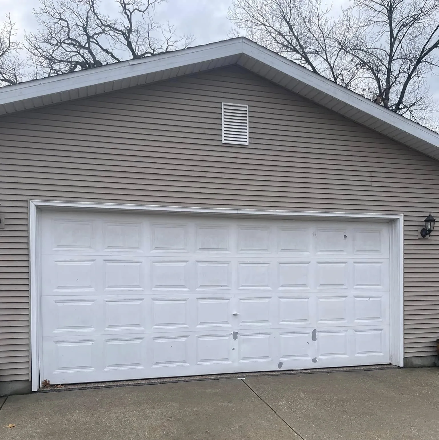 White two-car garage with beige siding and concrete driveway under cloudy sky
