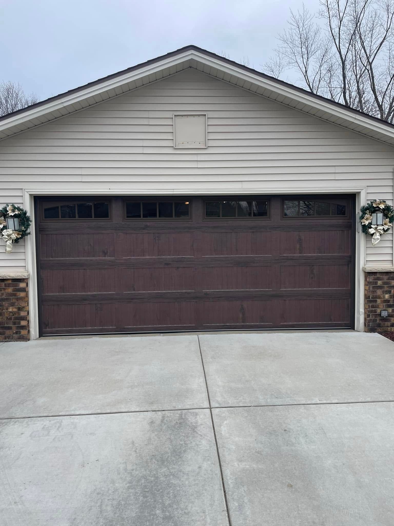 Two-car garage with a dark brown door, beige siding, and concrete driveway