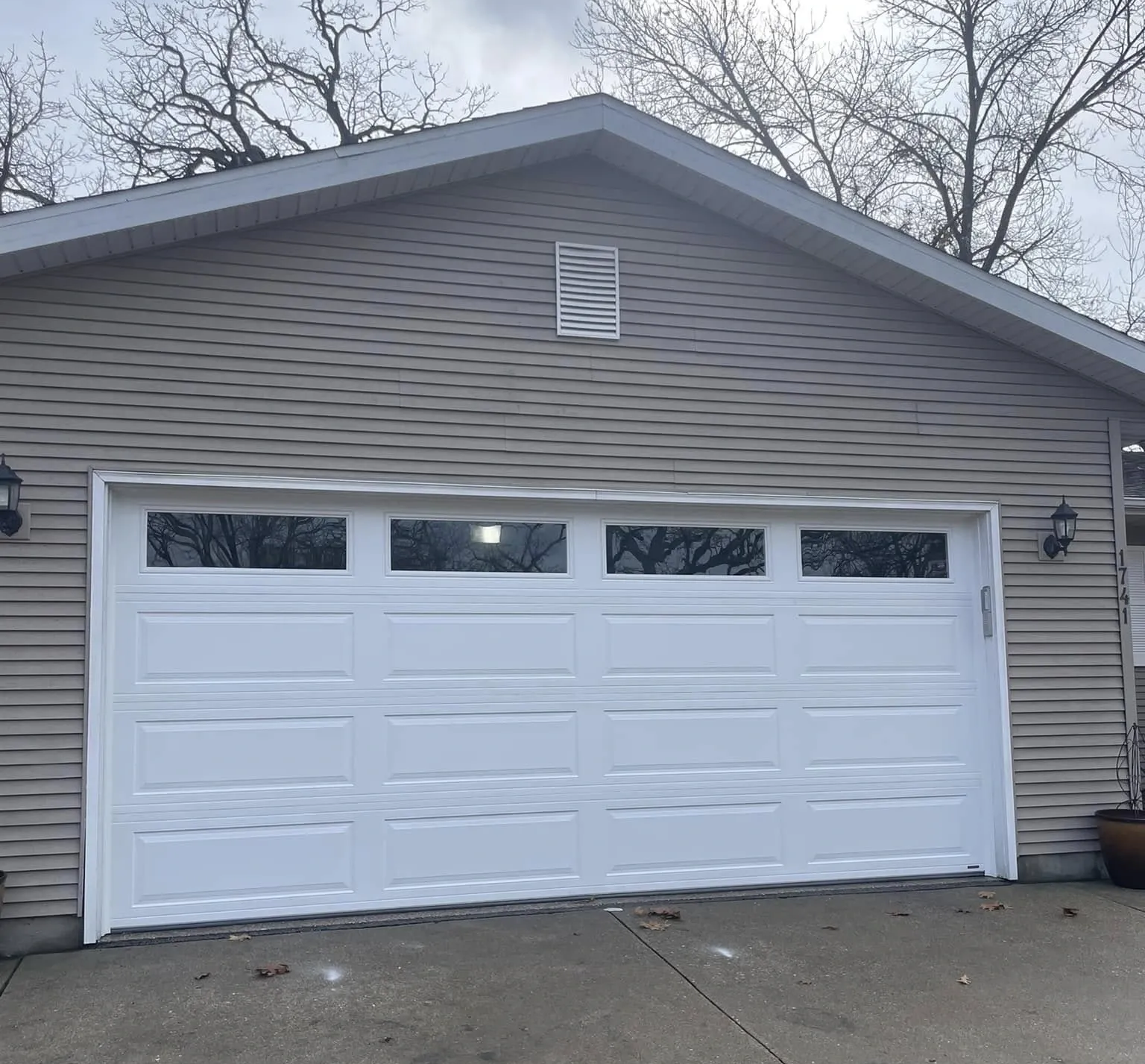 Gray house with white two-car garage door and concrete driveway under bare trees