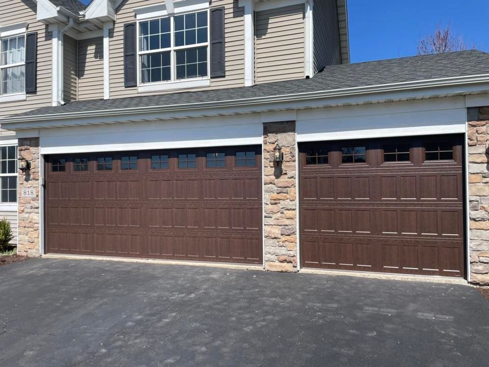 Two brown garage doors on a suburban townhouse with stone trim and a paved driveway