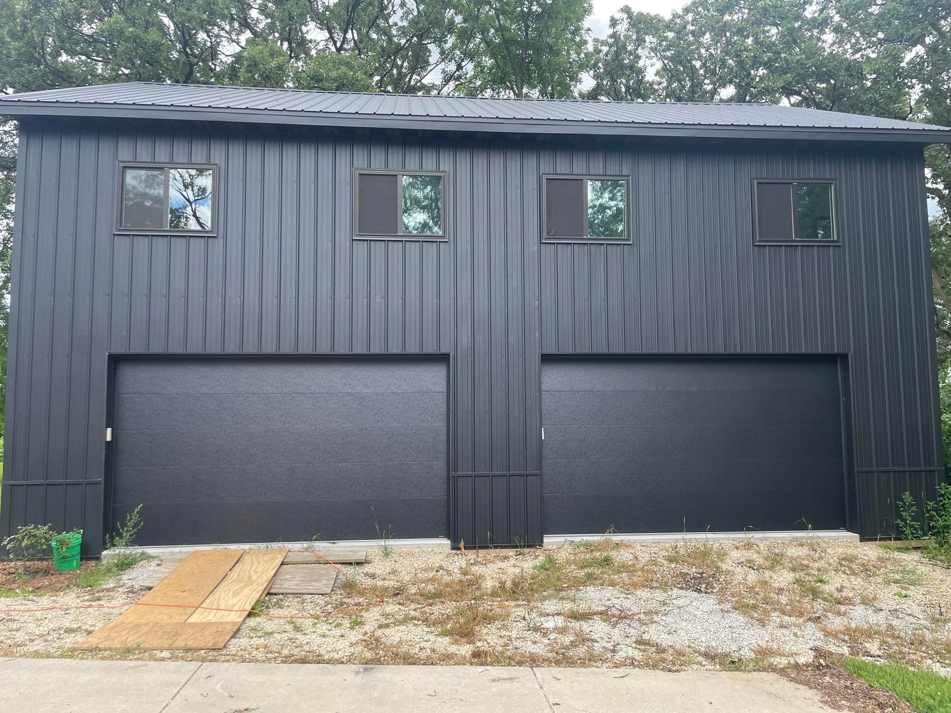 Black two-story garage with three windows and two large doors, viewed from the front.