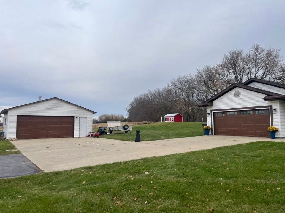 Two detached garages beside a wide concrete driveway and grassy yard under a cloudy sky