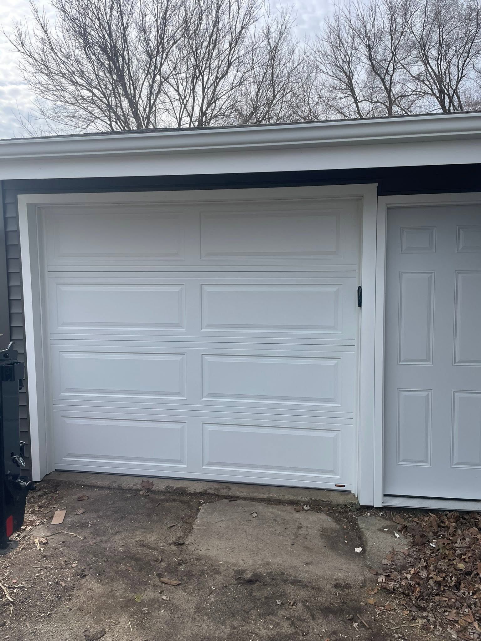 White garage door with visible damage under a carport roof, beside a driveway.