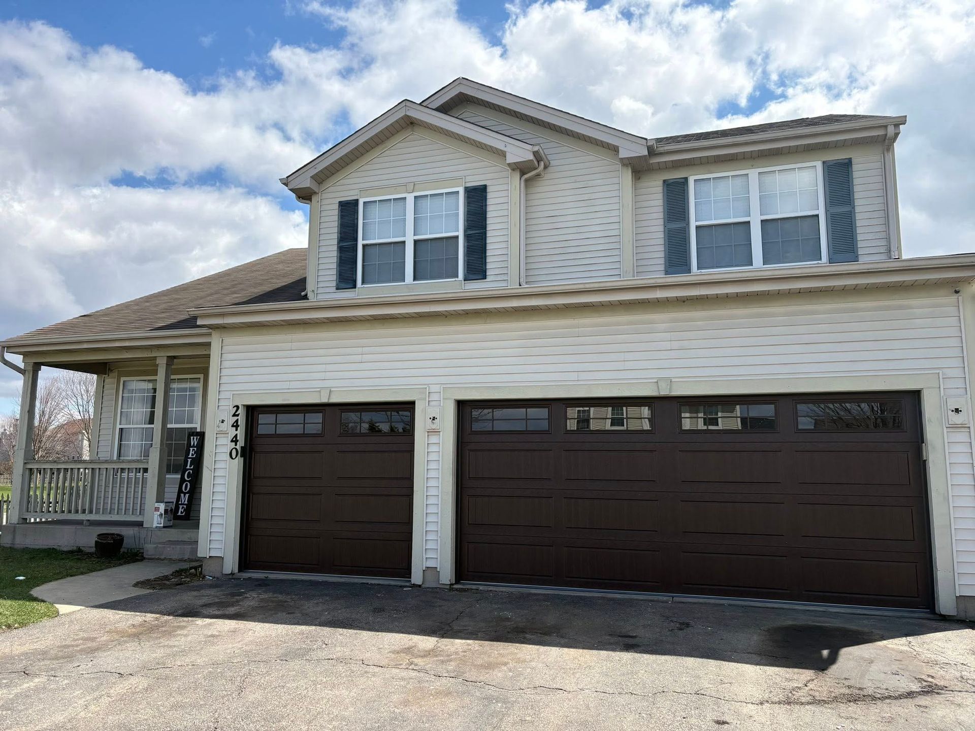 Suburban two-story beige house with a double dark-brown garage and cloudy sky