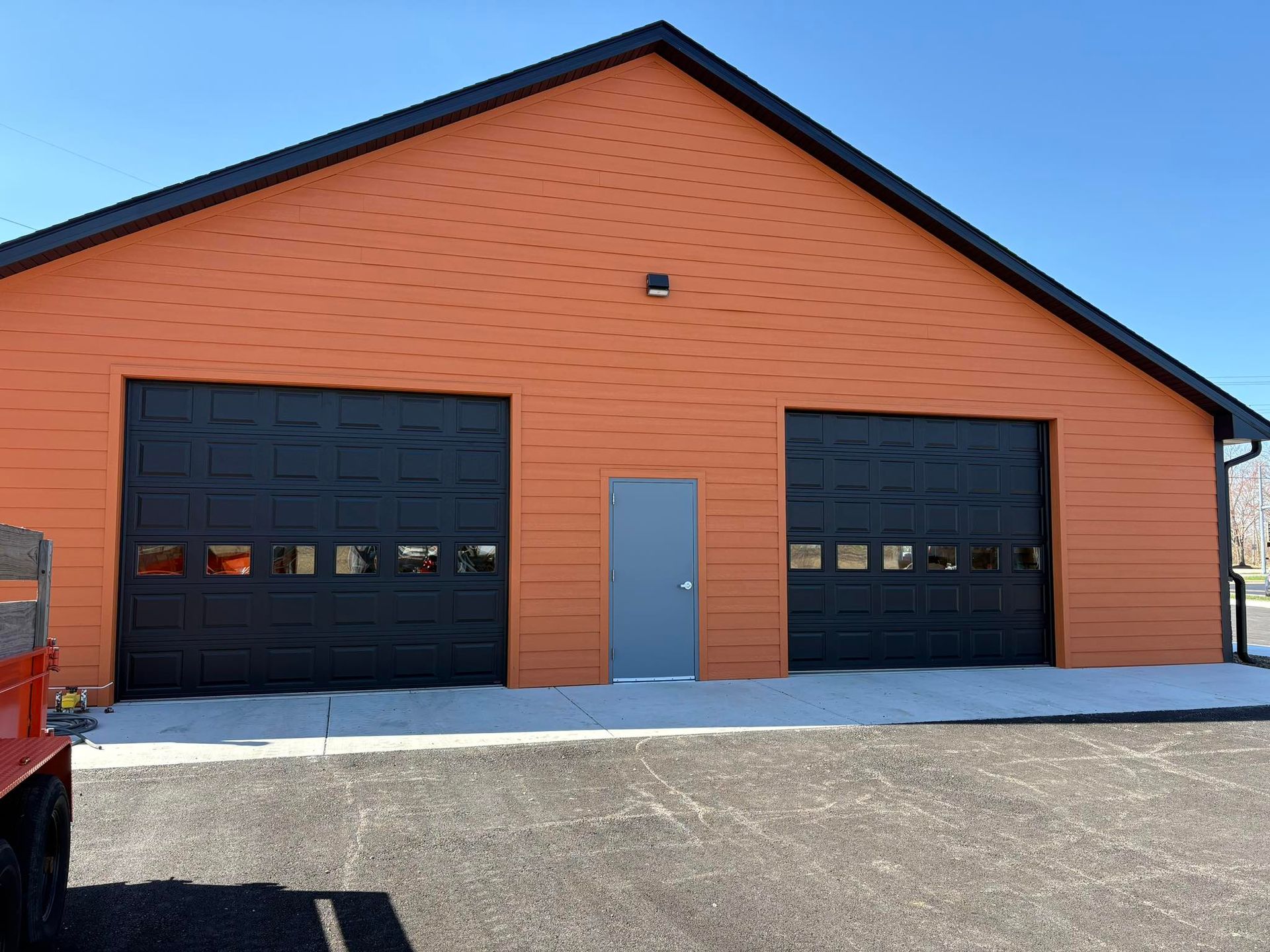 Orange brick building with two black garage doors and a gray side door under a peaked roof