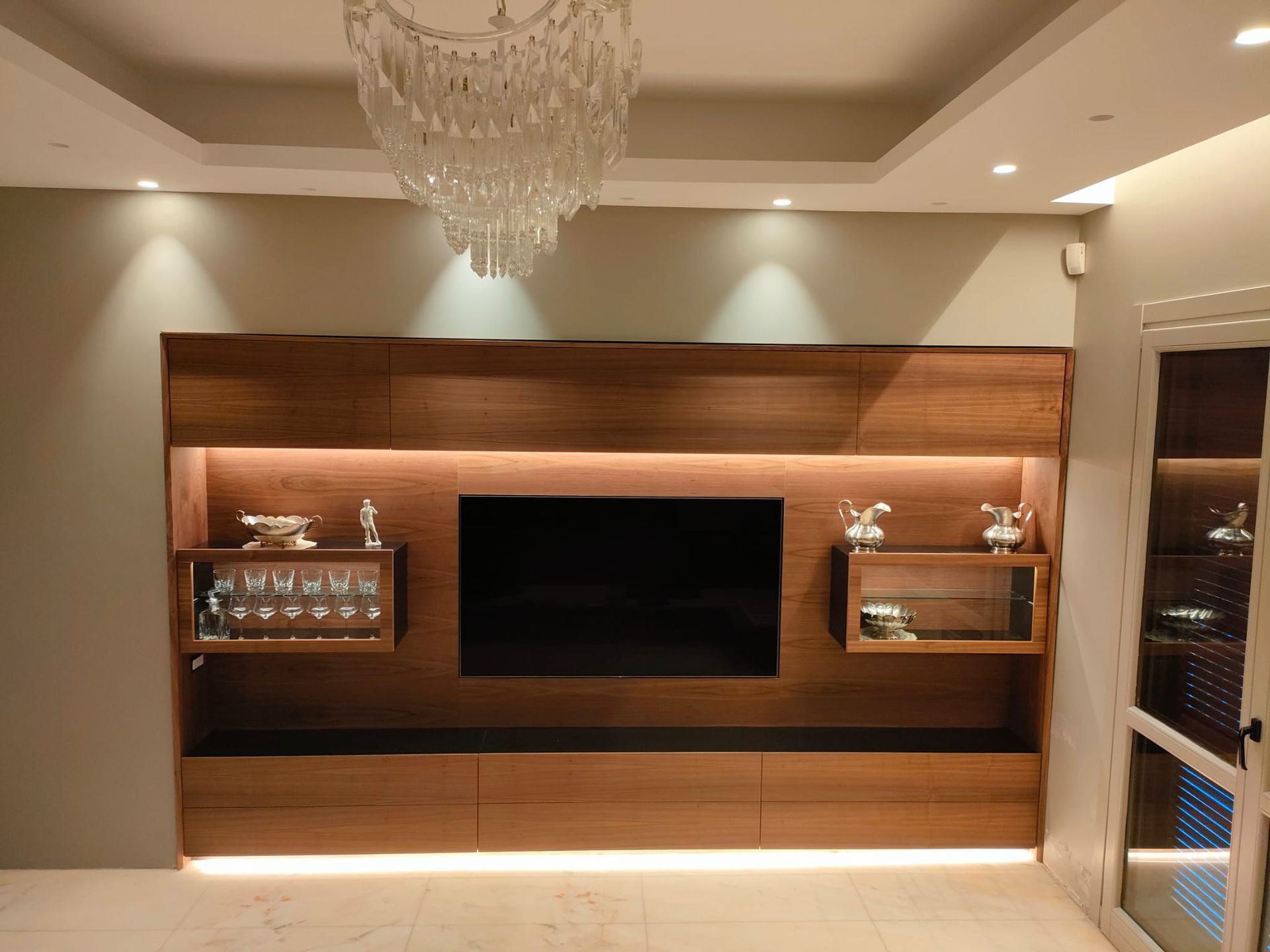 Un mobile per l'intrattenimento con pannelli in legno, ripiani integrati, illuminazione a LED e televisore montato a parete.