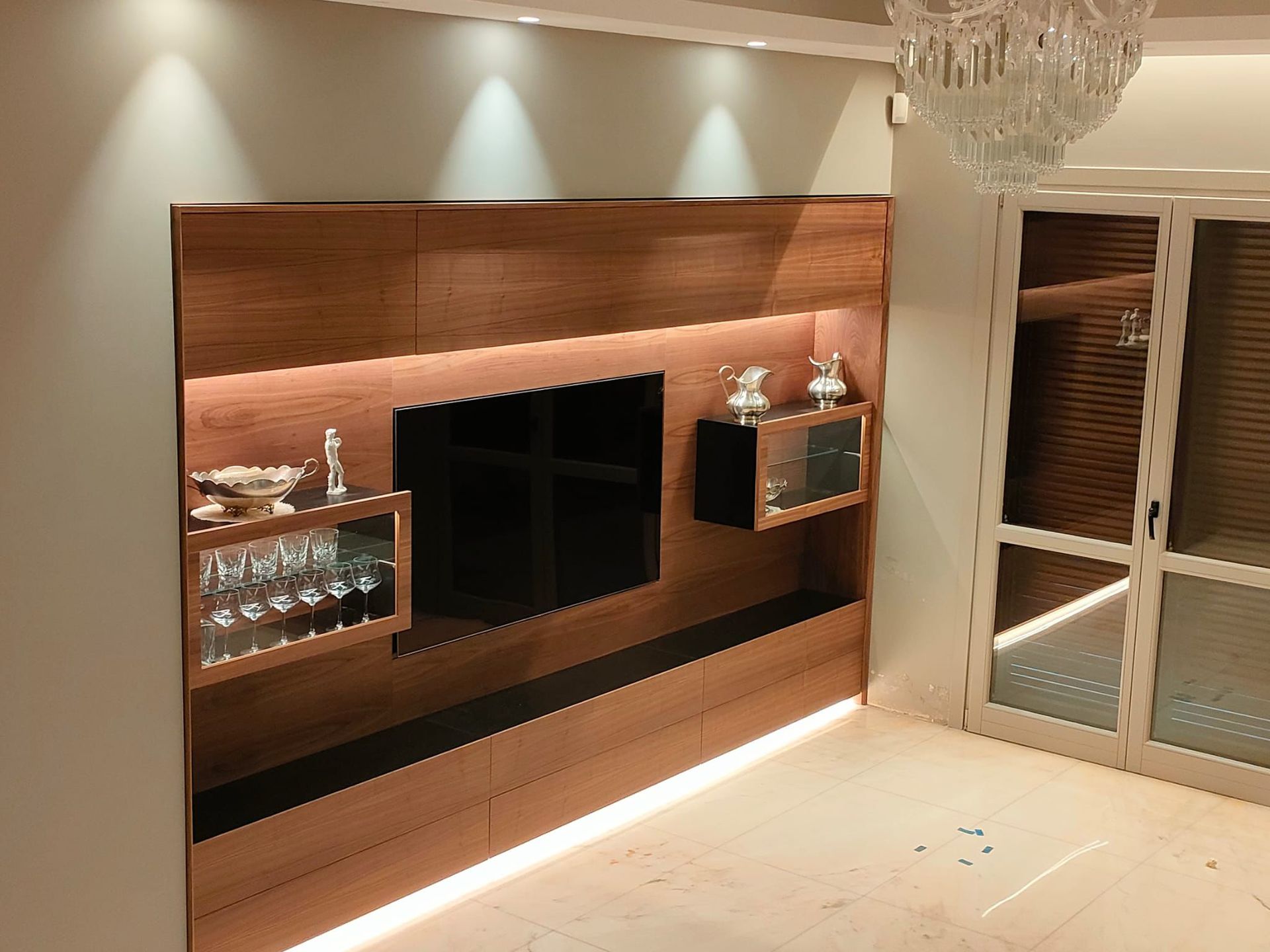 Una moderna parete multimediale con finitura in legno, dotata di televisore a schermo piatto, vetrine retroilluminate e illuminazione ambientale a LED a pavimento.