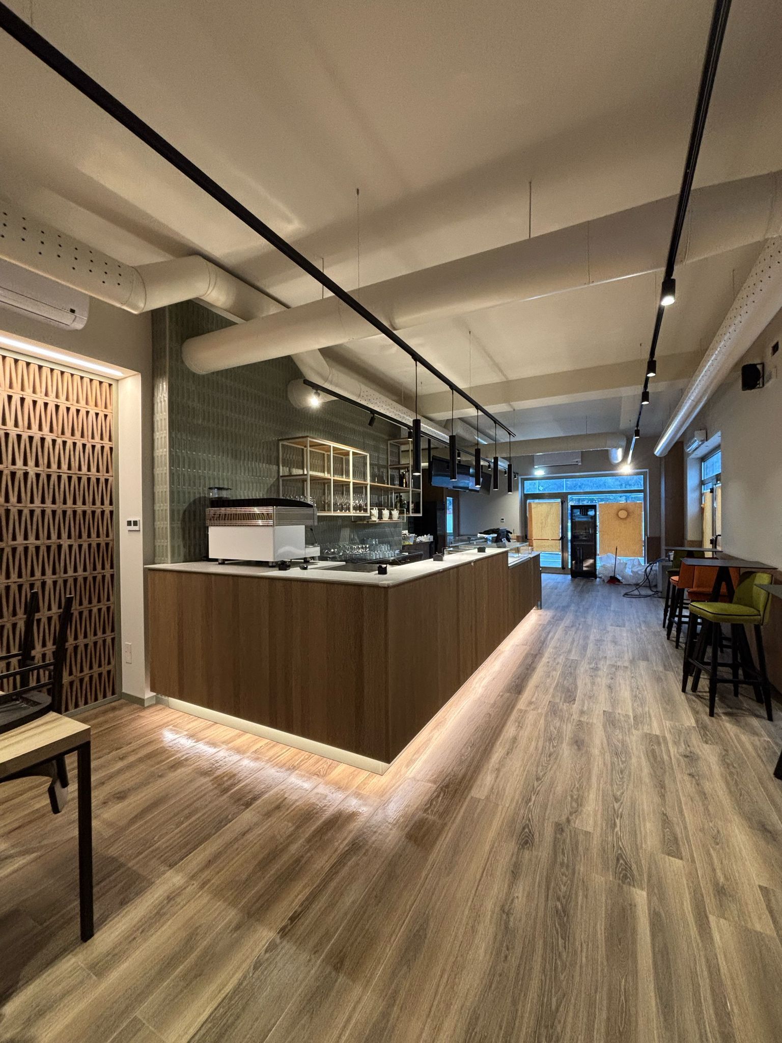 Interni moderni di una caffetteria con un lungo bancone di servizio rivestito in legno, illuminazione sottopensile e pavimento effetto legno.