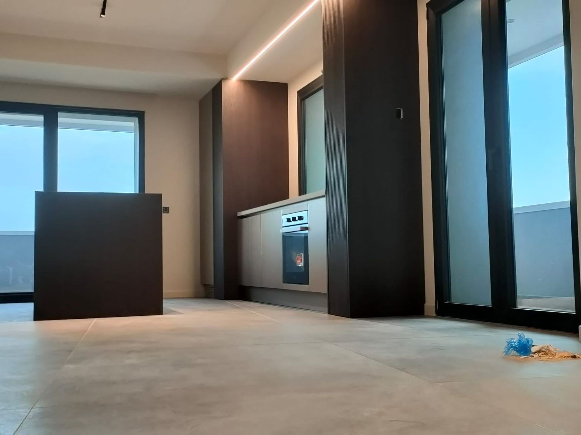 Una cucina moderna con mobili marroni, elettrodomestici in acciaio inossidabile e ampie finestre, vista da un pavimento piastrellato di colore chiaro.