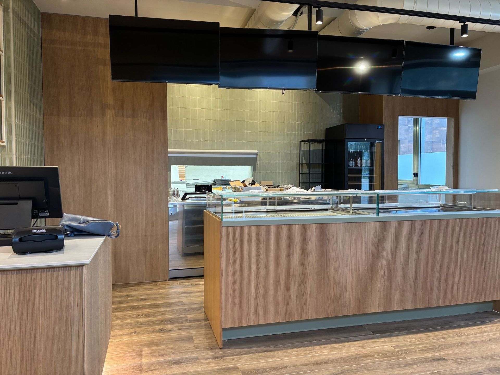 Interni moderni di una caffetteria con un lungo bancone di servizio rivestito in legno, illuminazione sottopensile e pavimento effetto legno.