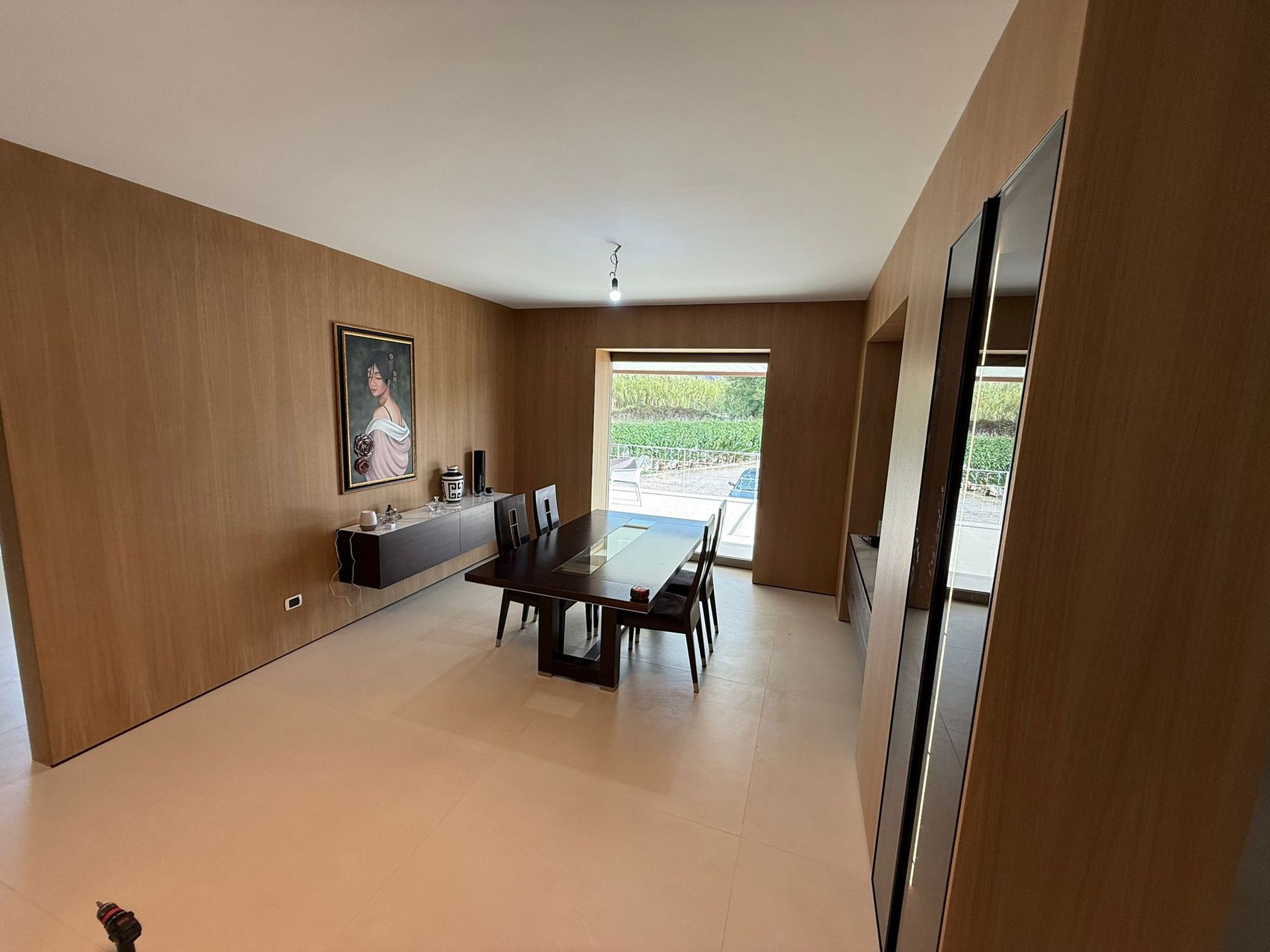 Sala da pranzo moderna con pareti rivestite in legno, un tavolo rettangolare scuro, sedie nere e un ritratto alla parete.